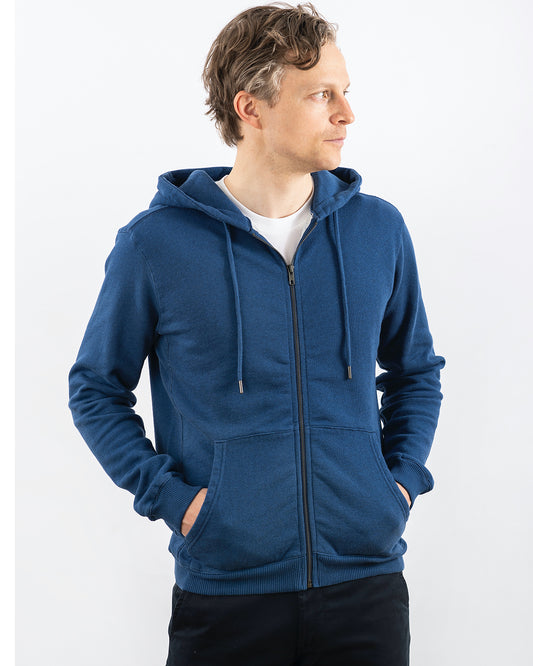A person wearing a blue melange zip hoodie with the hood up and the brand name 'Blankdays' visible on the embroidery at the neck.